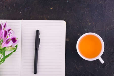 View from above. Fragrant tea in a white cup, beautiful flowers, a pink background, a notebook with a pen and glasses. Office.の写真素材