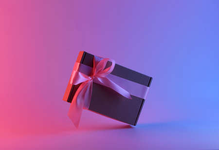 Gift box with a pink ribbon in neon light, with a pink and blue tintの写真素材