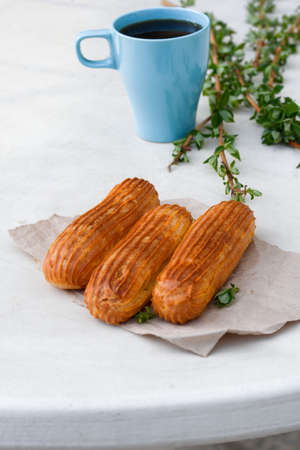 Aromatic coffee in a blue cup with eclairs in a summer cafe. Spring, cinnamon, leaf sprigs.