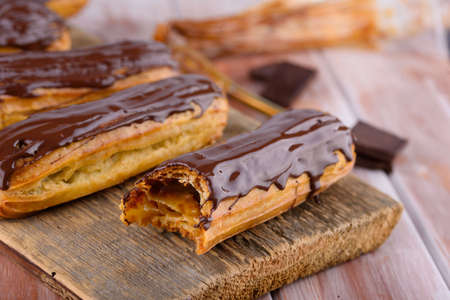 Tasty and beautiful eclairs with chocolate on a wooden board. Appetizing dessert. Party supplies....