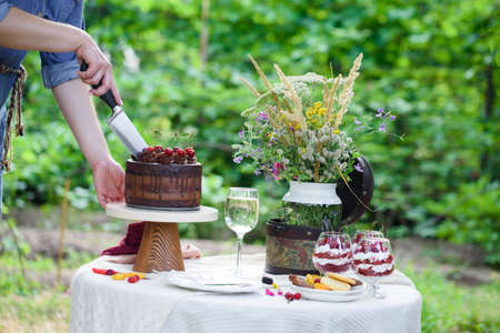 Delicious chocolate cake decorated with cherries with a glass of white wine, berries and wild flowers. Picnic in the countryの写真素材