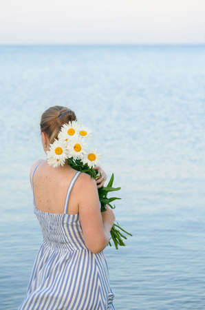 Beautiful summer photo. Girl in a walk on the sea with a flower in his hand. Summer and seaの写真素材