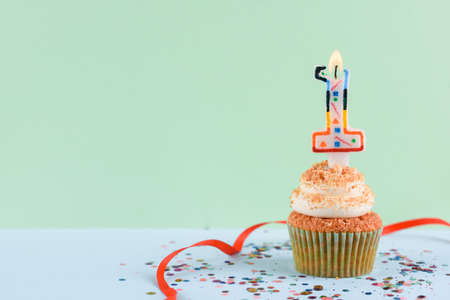 Beautiful festive cupcake on a light green background with sparkles and a single candle. Partyの写真素材