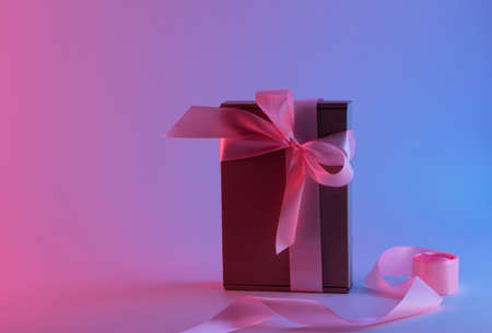 Gift box with a pink ribbon in neon light, with a pink and blue tintの写真素材