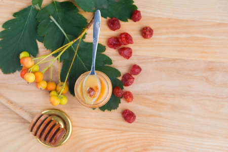 Tasty and aromatic honey in a jar with rowan berries and viburnum on a wooden table. View from above