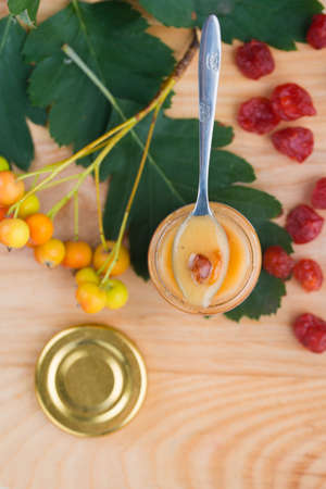 Tasty and aromatic honey in a jar with rowan berries and viburnum on a wooden table. View from above