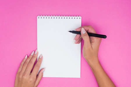 Notebook with pen holds female hands on a pink background. Flat layの写真素材