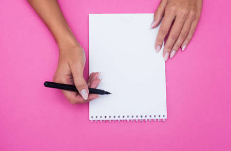 Notebook with pen holds female hands on a pink background. Flat layの写真素材