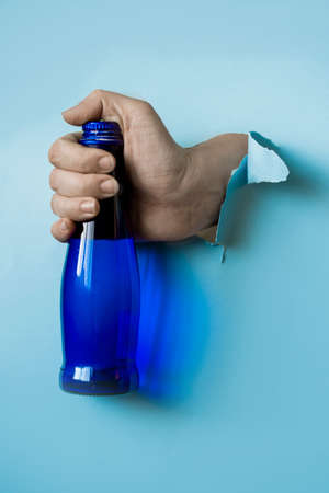 A hand holds a blue water bottle from a torn paper hole. Trend torn paper.の写真素材