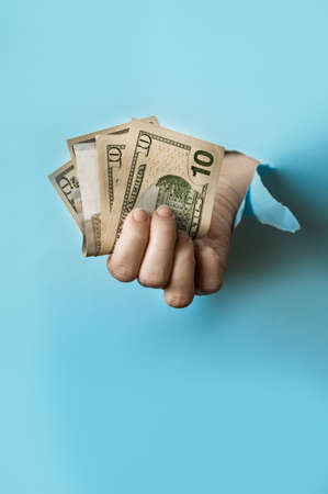 A hand holds a money on the blue torn paper hole. Trend torn paper.の写真素材