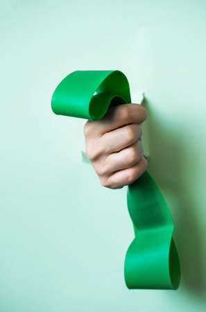 A hand holds a sports green rubber band exercise machine for sports through torn paper. Trend torn paperの写真素材