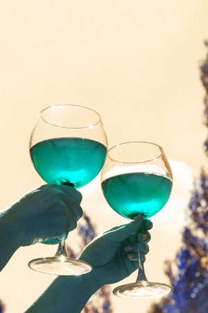 Two glasses with wine in hand against the sky in neon tinted. Mint colourの写真素材