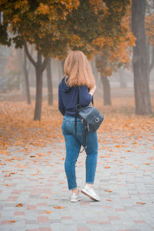Girl with a backpack in a beautiful foggy autumn in the park with yellow leaves turned her back to the frame.の写真素材