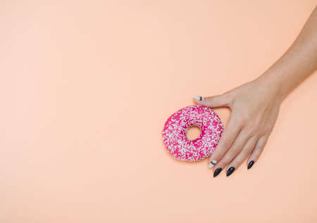 Appetizing donuts with icing on a colored background with female hands with a beautiful manicure.の写真素材