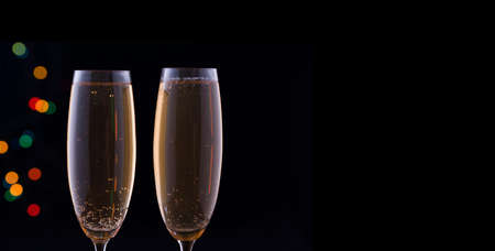 Two glasses with champagne with festive lights on a dark background. New Year contentの写真素材