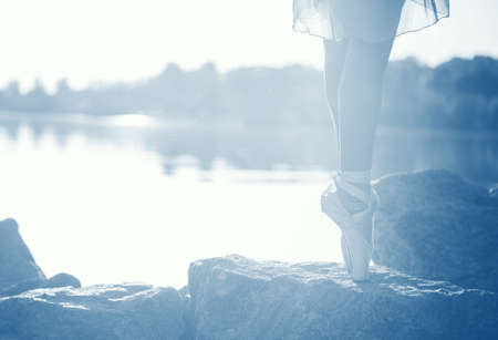 Beautiful legs of a ballerina on the seashore on the stones, at sunset, in the tinted fashion color...