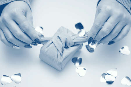 Gift in female hands with a beautiful manicure. Gift in ecological packaging - Furoshiki. Festive...