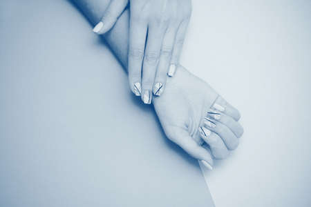 Beautiful female hand with trendy nail art manicure on a blue background. Place for an inscription.の写真素材