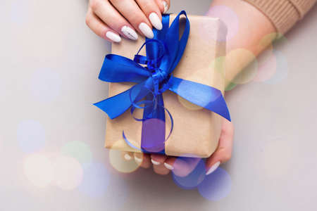 Beautiful stylish female manicure on a gray background with gift in hand. Art content