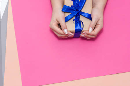 Beautiful stylish female manicure on a pink background with gift in hand. Holidays giftの写真素材
