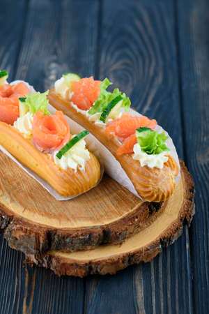 Tasty and beautiful eclairs on a wooden board. Appetizing dessert with red fish, cucumber, cheese and greens. With black wood .の写真素材