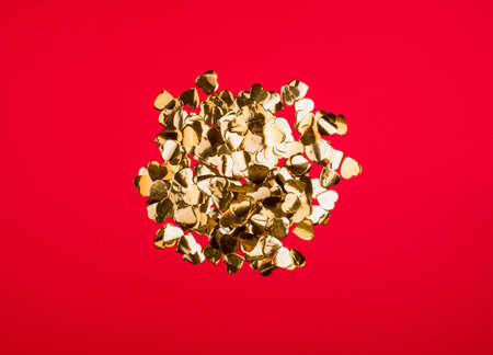Golden candy in the form of small hearts on a bright red background. Abstract contentの写真素材