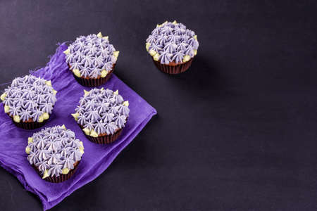 Delicate chocolate cupcakes close-up on a dark table with a napkin. Color tasty cream with little flowersの写真素材