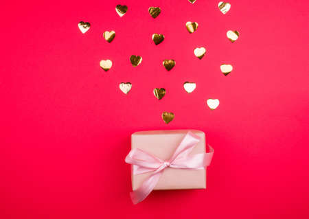 Beautiful gift box with satin ribbon of delicate pink color, with golden confetti on a red...