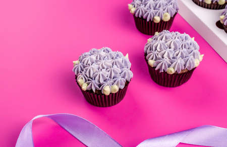 Delicious shawn cupcakes with curd cream in the form of flowers on a pink background. White cupcake packaging.の写真素材