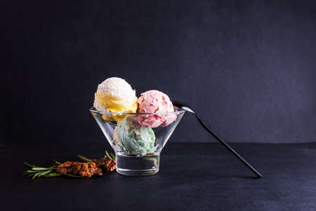 Three colorful balls of delicious ice cream, on a black background with nuts and a sprig of mint. Copy spaceの写真素材