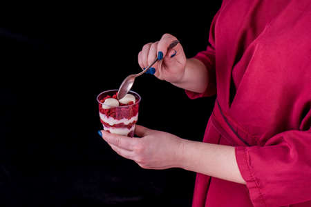 Dessert red velvet in a small transparent cup. The girl's hands on a dark background. Spoon with cake.の写真素材