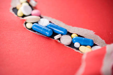 Lots of different pills in torn red paper. Medicines against diseaseの写真素材