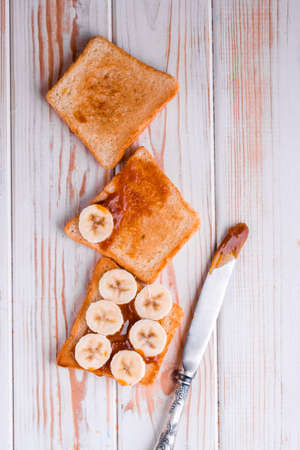 Two delicious toasts with salted caramel and bananas on the table. A healthy breakfast with milk.