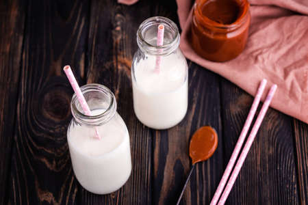 Two bottles of fresh milk with tubes and fresh homemade salted caramel on dark background. Delicious breakfastの写真素材