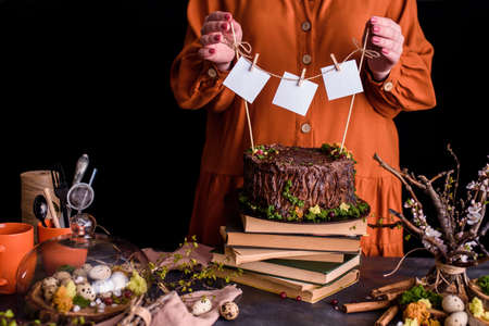 Beautiful composition with cake, books, cups, eggs, flowers, twigs. The girl attaches a thread to...