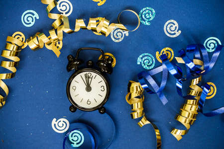 Black clock alarm clock among gold osperpantin, sequins on a blue background. Holiday content.の写真素材