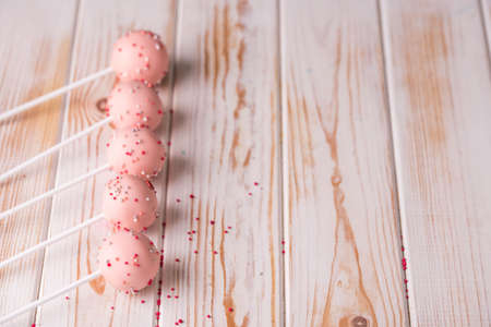 Dessert on a stick. Pink cake pops with a sprinkle on a wooden background. Tasty food