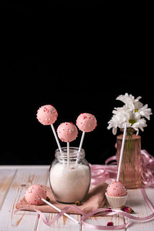 Pink cake pops in a jar of sugar in the form of a bouquet on a wooden background. Tasty desserts