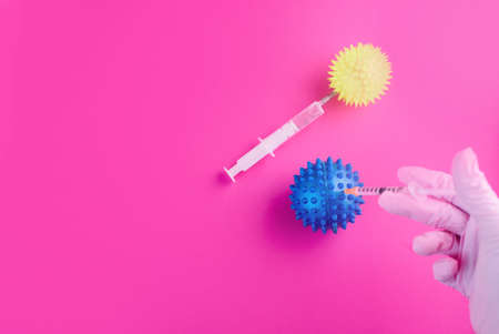 The hand in the gloves holds a syringe and injects the virus. Content for coronavirus on a pink background. COVID-19の写真素材