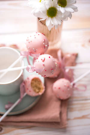 Cake pops in a light key in a beautiful utensil with pink chocolate cream and flowers on a wooden background. Tasty foodの写真素材