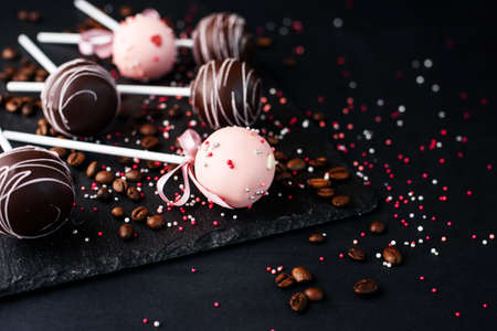 Delicious dessert with chocolate and milk cream on a stick with an atal tape. Cake pops on a slate board on a black background with coffee beans.の写真素材
