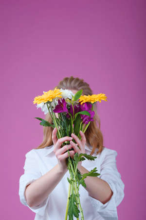 The girl on a pink background holds a beautiful bouquet of different flowers and covers her face. Trend photo without face.の写真素材