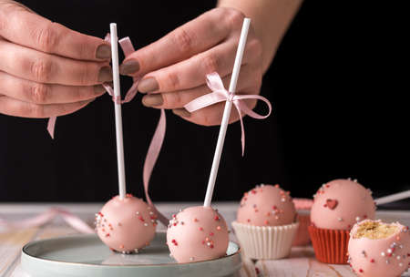 The pastry chef decorates cake pops with satin ribbons. Desserts with pink cream. Tasty food