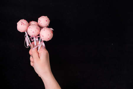 Cake pops in womens hands on a black background. Dessert in pink chocolate cream with powder and bow.の写真素材