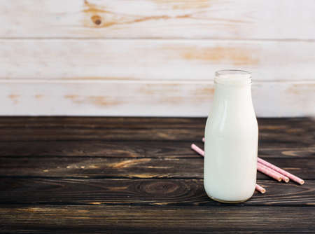 Fresh milk, in a glass bottle on a black wooden background with pink drink tubes.fresh drinkの写真素材