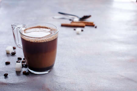 Delicious and fragrant coffee with a glass cup of milk, sticks of fragrant cinnamon, coffee beans, sugar cubes, on the tableの写真素材