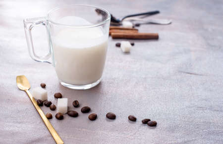 Delicious and fragrant coffee with a glass cup of milk, sticks of fragrant cinnamon, coffee beans, sugar cubes ob the tableの写真素材
