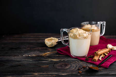 Delicious and fragrant dalgona coffee in glass cups, cinnamon sticks, dried mushrooms, a spoon of instant coffee, sugar. Cooling coffee drink with milkの写真素材