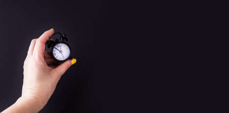 The hand holds a small alarm clock on a black background, a place for text. Contentの写真素材