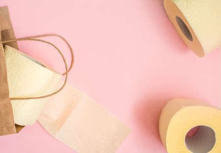 Three rolls of toilet paper with a craft bag for shopping and goods on a pink background. Place for text, view from above.の写真素材